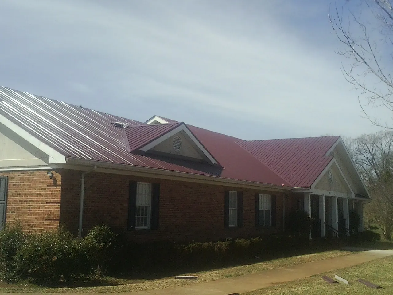 Red metal roof with gabled entries on a long brick building, from a Hail Damage Roof Repair job in Whitesboro