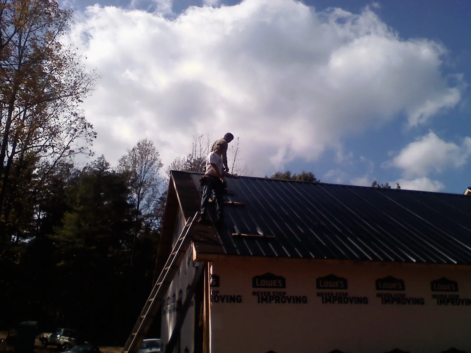 Roofer fastening dark metal panels high against a cloudy sky in Whitesboro